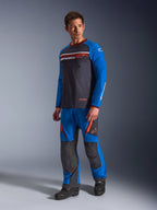 Alpinestars Maxdura Dual Jersey, donkergrijs en koningsblauw, adventure motortrui met een mesh torso en koningsblauwe mouwen, gedragen door een model met bijpassende off-road rijbroek, voorzien van borstzakken met ritssluiting en Alpinestars-branding.