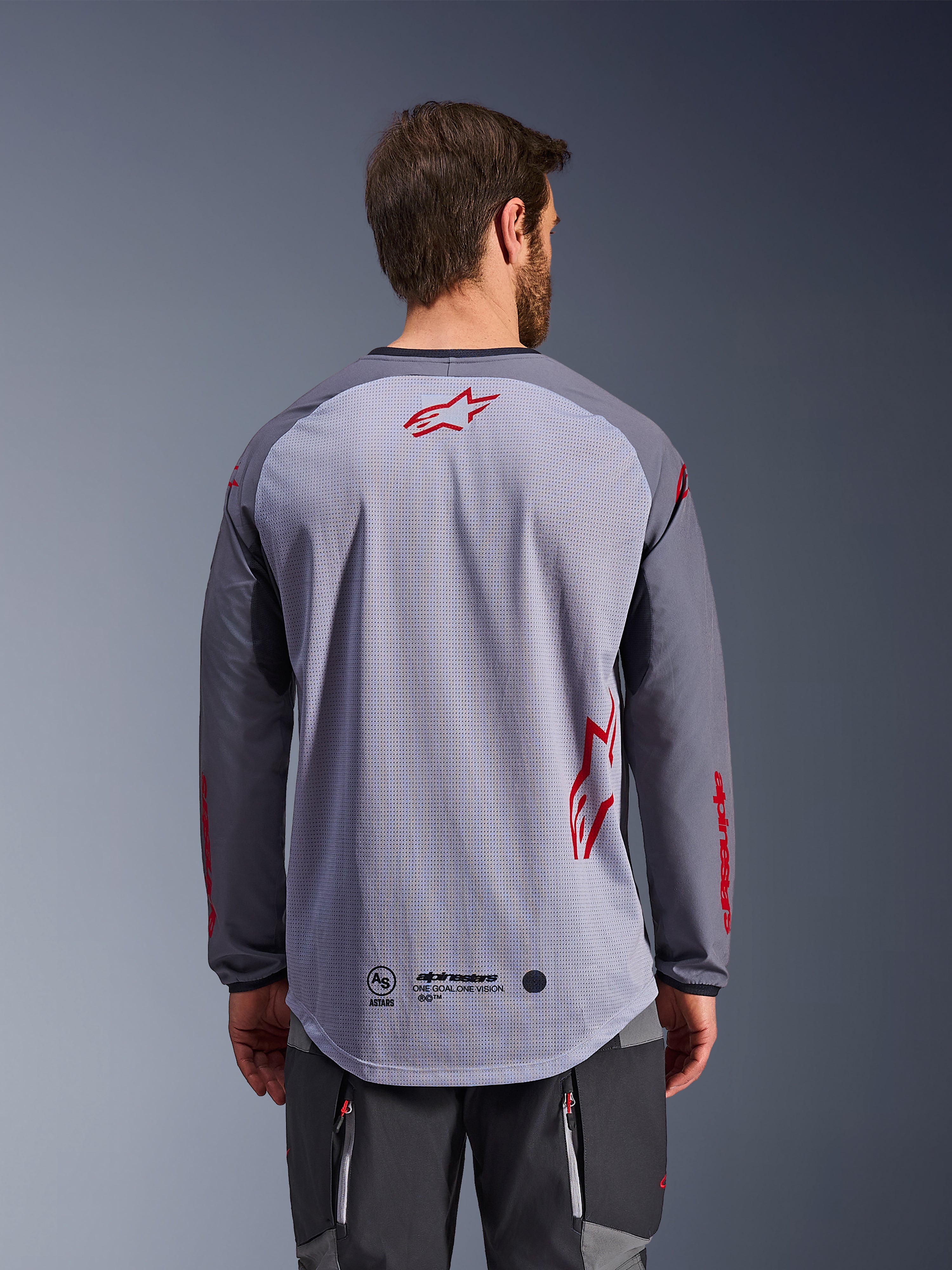 Alpinestars Maxdura Dual Jersey, achteraanzicht, middengrijs en donkergrijs, met een ademende mesh achterkant met rode Alpinestars sterlogo's, lange mouwen en een verlengde drop-tail zoom, adventure motorkleding