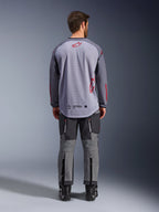Mannelijk model van achteren gezien die de Alpinestars Maxdura Dual Jersey draagt, grijs en donkergrijs adventure-shirt met rode logo-accenten, mesh rugconstructie, gedragen met bijpassende grijze off-road broek en zwarte laarzen.