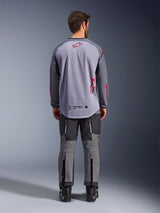 Male model from behind wearing the Alpinestars Maxdura Dual Jersey, Mid Gray and Dark Gray adventure jersey with red logo accents, mesh back construction, worn with matching gray off-road pants and black boots
