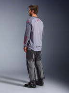 Man die een Alpinestars Maxdura Dual Jersey draagt, lichtgrijs met rode Alpinestars-logo's, achteraanzicht met mesh torso en lange mouwen, gecombineerd met een antracietgrijze technische broek en zwarte motorlaarzen
