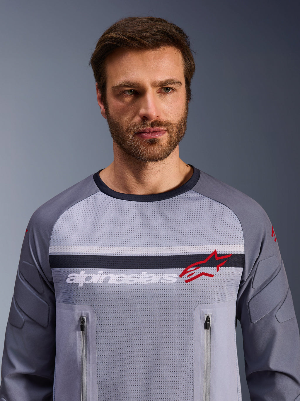 Alpinestars Maxdura Dual Jersey, midden-grijs en donkergrijs, gedragen door mannelijk model, voorzien van een mesh torso voor ventilatie, dubbele borstzakken met ritssluiting, witte 'alpinestars' branding en rood ster-logo, hoogwaardige off-road adventure uitrusting