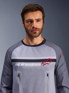 Alpinestars Maxdura Dual Jersey, midden-grijs en donkergrijs, gedragen door mannelijk model, voorzien van een mesh torso voor ventilatie, dubbele borstzakken met ritssluiting, witte 'alpinestars' branding en rood ster-logo, hoogwaardige off-road adventure uitrusting