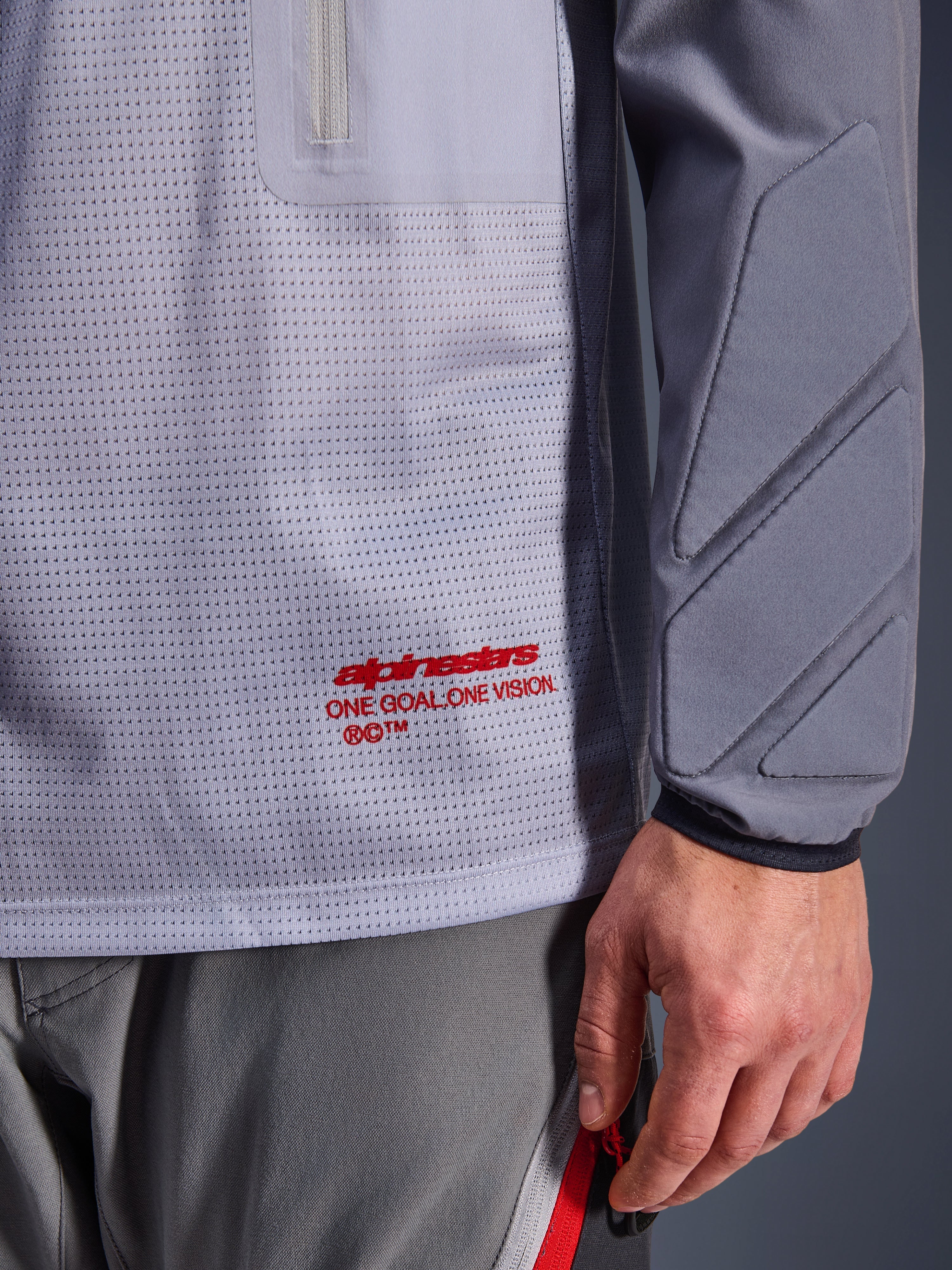 Alpinestars Maxdura Dual Jersey, middengrijs en donkergrijs, close-up van de ademende mesh torso met rode branding, detail van de zak met ritssluiting en geïntegreerde padding op de mouw, technische adventure motorkleding