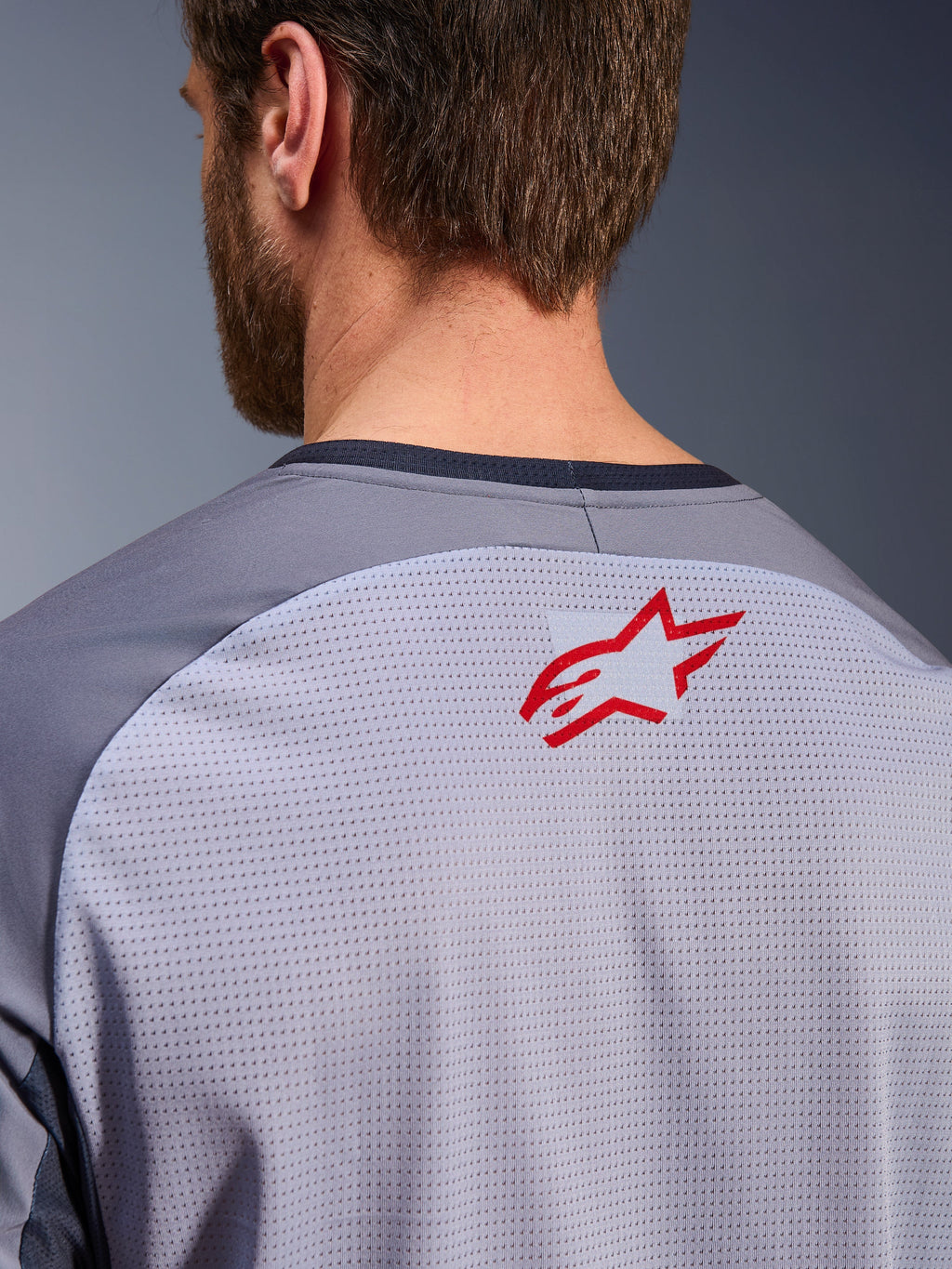 Alpinestars Maxdura Dual Jersey in Mid Gray en Dark Gray, close-up van de bovenrug en kraag, voorzien van een klein rood Alpinestars sterlogo op ademende lichtgrijze mesh-stof met donkergrijze nektrim, ontworpen voor adventure off-road rijden
