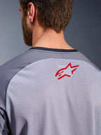 Alpinestars Maxdura Dual Jersey in Mid Gray en Dark Gray, close-up van de bovenrug en kraag, voorzien van een klein rood Alpinestars sterlogo op ademende lichtgrijze mesh-stof met donkergrijze nektrim, ontworpen voor adventure off-road rijden