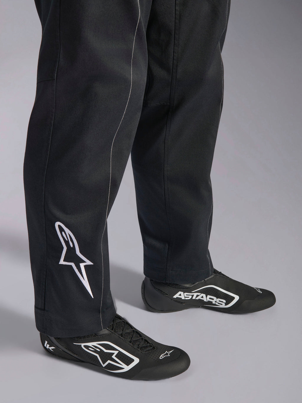 Alpinestars Kart Indoor V2 Pak, zwart kartingpak, close-up van de onderbenen en voeten met een wit Alpinestars-logo op de kuit, gedragen met bijpassende zwart-witte raceschoenen, ontworpen voor recreatief karten
