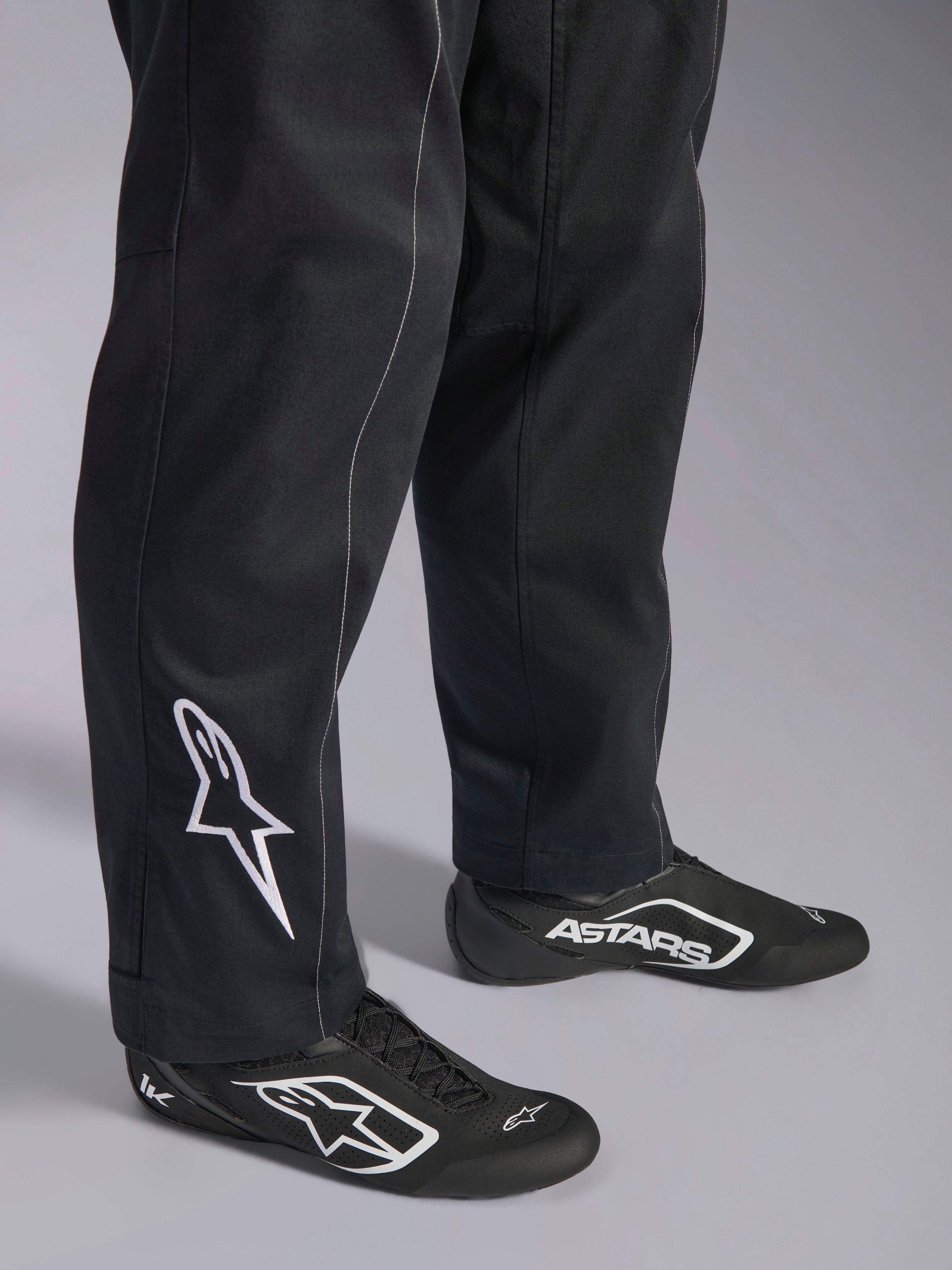 Alpinestars Kart Indoor V2 Pak, zwart kartingpak, close-up van de onderbenen en voeten met een wit Alpinestars-logo op de kuit, gedragen met bijpassende zwart-witte raceschoenen, ontworpen voor recreatief karten