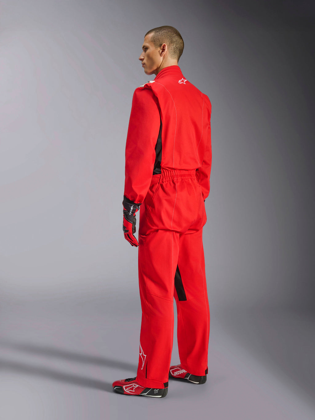 Alpinestars Kart Indoor V2 Suit, rood kartpak, driekwart achteraanzicht op een model, gedragen met bijpassende rode handschoenen en raceschoenen, enkellaagse poly-katoen keperconstructie, professionele motorsportuitrusting voor indoor karten