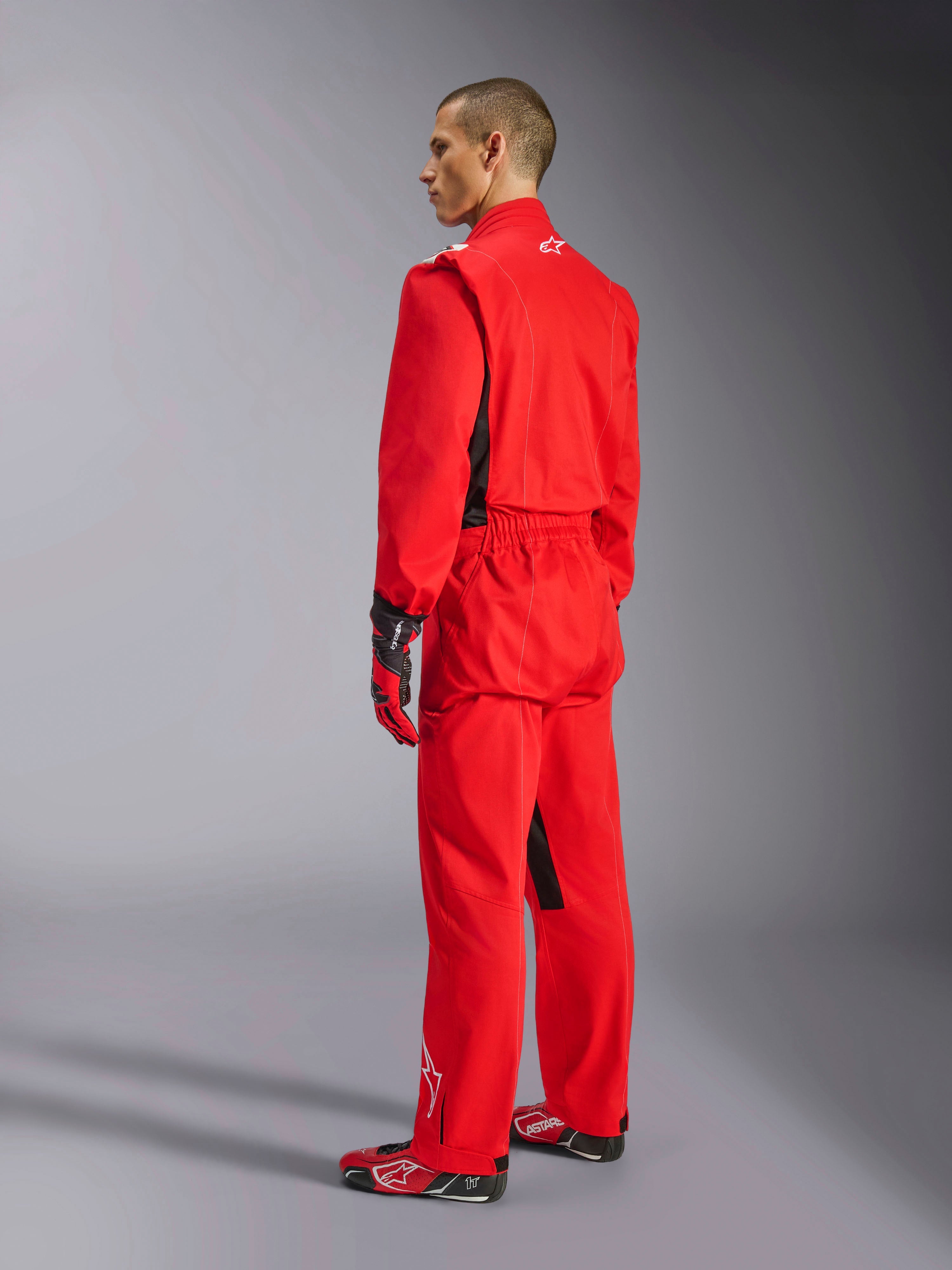 Alpinestars Kart Indoor V2 Suit, rood kartpak, driekwart achteraanzicht op een model, gedragen met bijpassende rode handschoenen en raceschoenen, enkellaagse poly-katoen keperconstructie, professionele motorsportuitrusting voor indoor karten