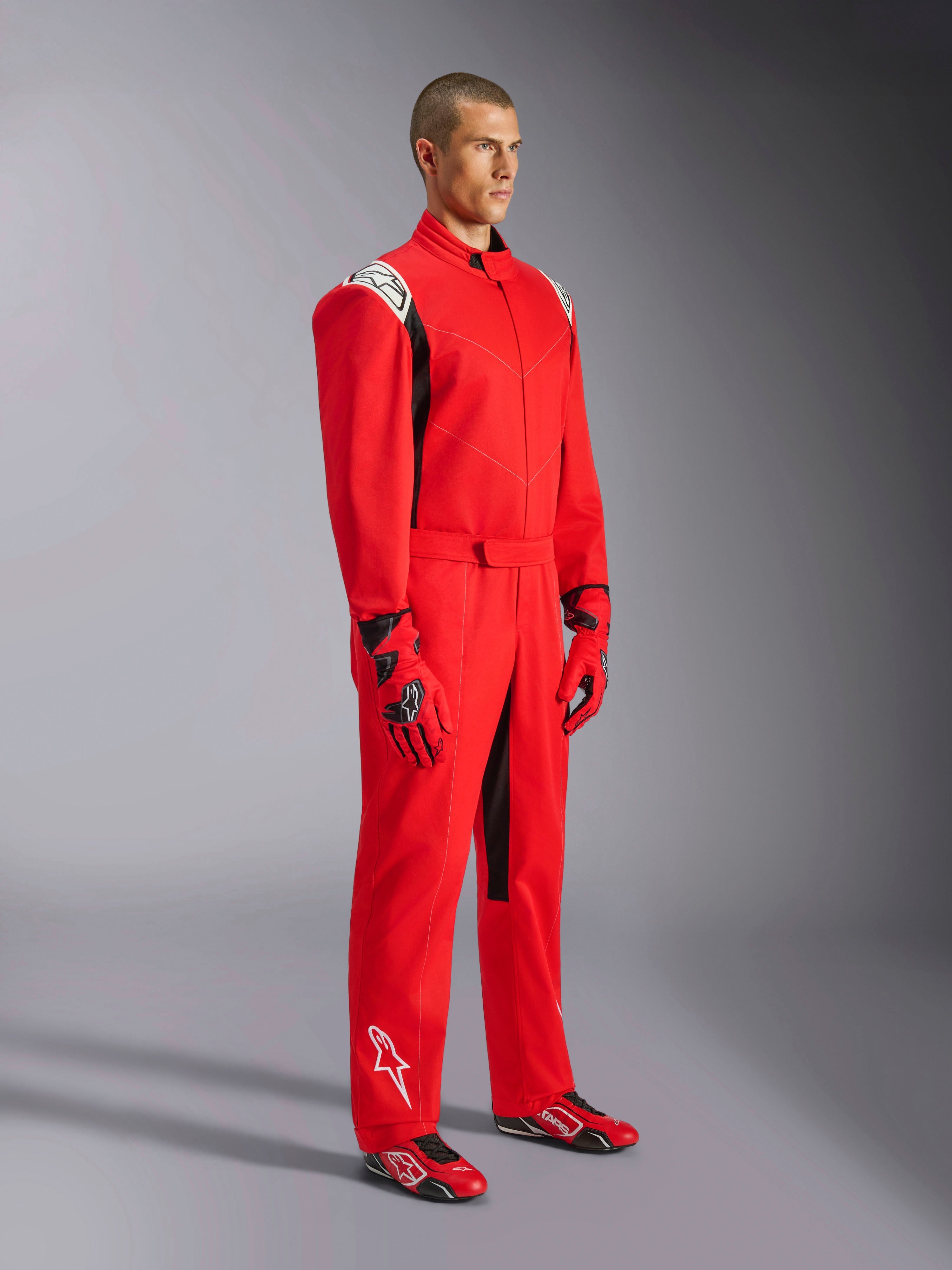 Alpinestars Kart Indoor V2 Suit, rood kartingpak, gedragen door een model met bijpassende rode en zwarte handschoenen en schoenen, met witte logo's op de schouders en het onderbeen, zwarte accenten, ontworpen voor recreatief karten en indoorbanen