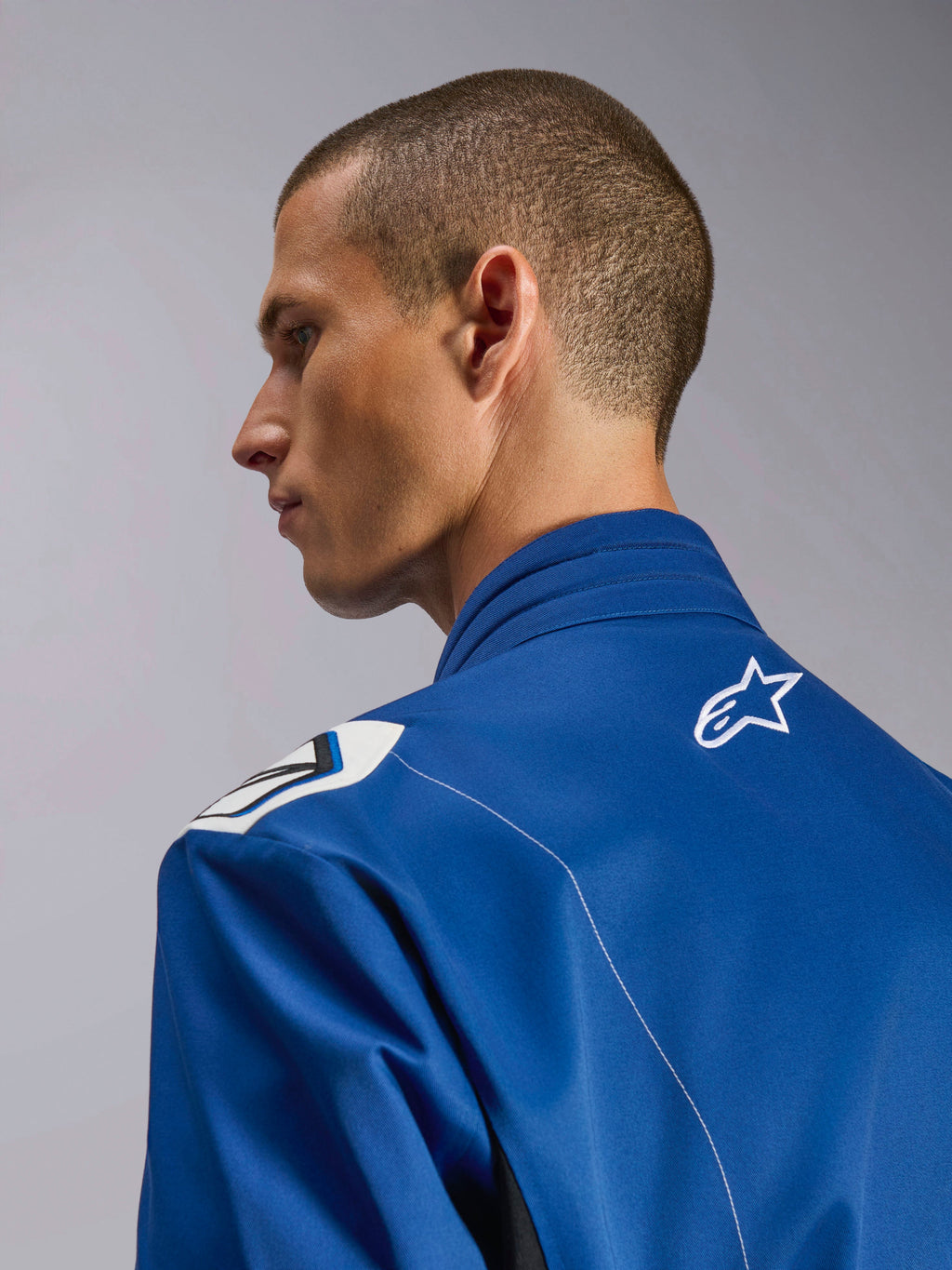 Alpinestars Kart Indoor V2 Suit, blauw kartpak, close-up zijprofiel van de ergonomische kraag en bovenrug met wit sterlogo, voorzien van een op de Formule 1 geïnspireerd schouderontwerp en een duurzame poly-katoen keperconstructie