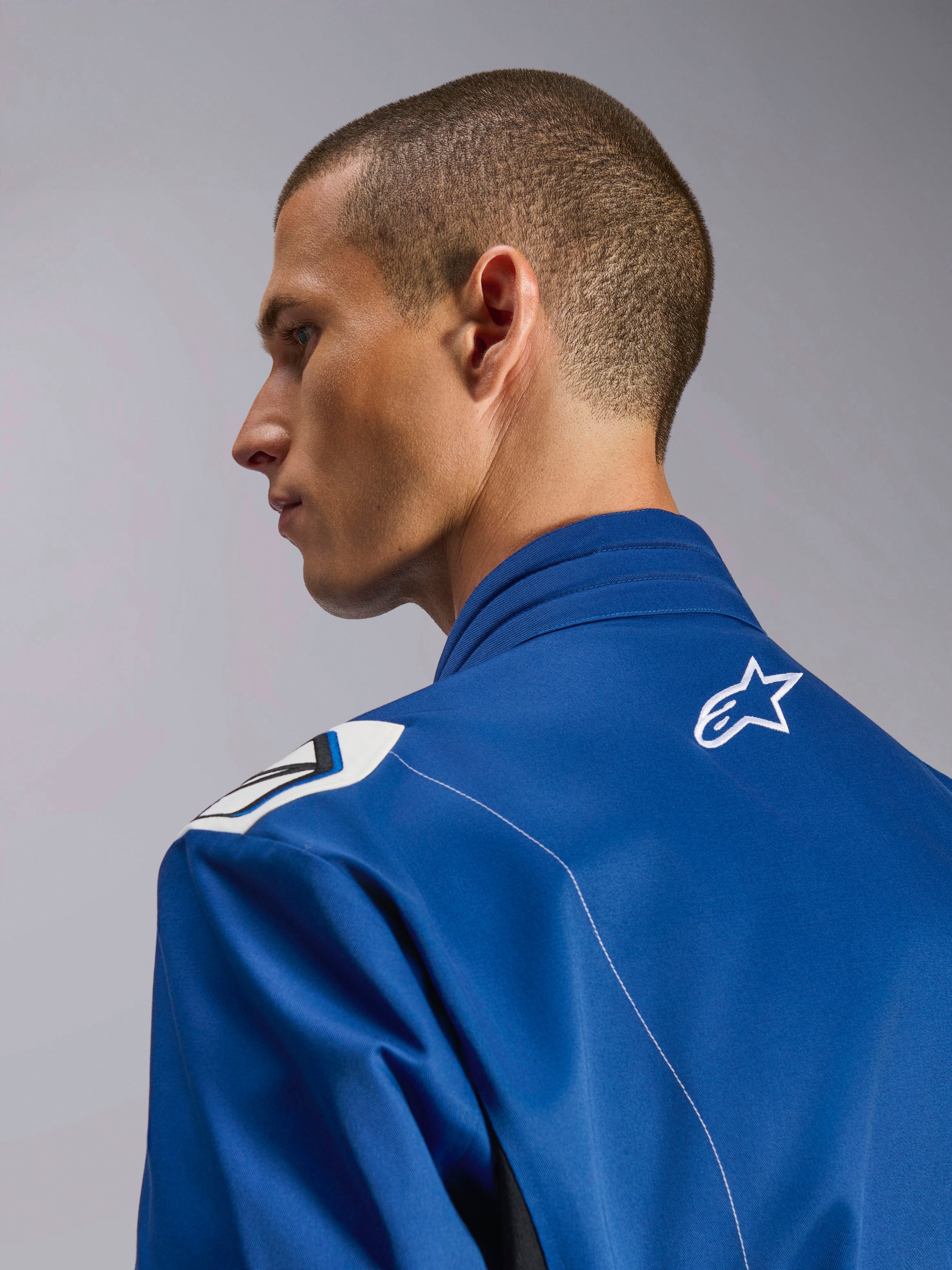 Alpinestars Kart Indoor V2 Suit, blauw kartpak, close-up zijprofiel van de ergonomische kraag en bovenrug met wit sterlogo, voorzien van een op de Formule 1 geïnspireerd schouderontwerp en een duurzame poly-katoen keperconstructie
