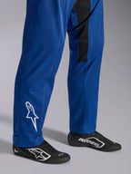 Alpinestars Kart Indoor V2 Pak, blauw, close-up van de onderbenen en voeten met wit sterlogo op de enkel, verstelbare broekspijpen en zwarte raceschoenen, duurzame kartkleding voor recreatief gebruik op het circuit