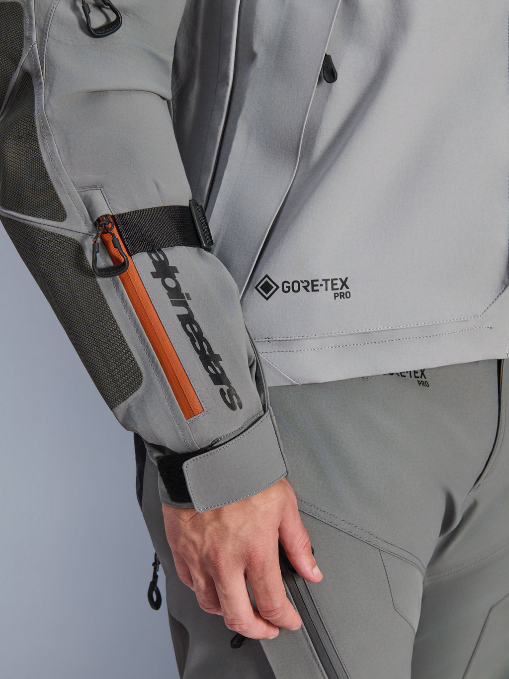 Alpinestars Nazca 3L GORE-TEX PRO Jas, donkergrijze en middengrijze adventure jas, close-up detail van mouw met zwarte merkdetails en oranje ritsaccent, GORE-TEX PRO-logo op de torso, duurzame textielconstructie met versterkt elleboogstuk