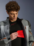 Mannelijk model draagt Alpinestars Nazca 3L GORE-TEX PRO jas, donkergrijs en middengrijs, toont rode Nucleon PLASMA Pro protector-inzet, adventure motorkleding, premium motorjas met technische details