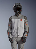 Alpinestars Nazca 3L GORE-TEX PRO jas, adventure motorjas, donkergrijs en middengrijs met oranje ritsaccenten, gedragen met bijpassende broek en zwarte helm, duurzame textielconstructie met zichtbare GORE-TEX PRO- en All Terra-branding