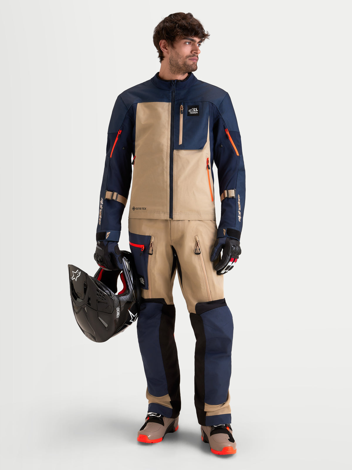Alpinestars Arenis Gore-Tex Jacket, men's adventure touring motorcycle jacket in night navy blue and aluminum beige, worn by a model holding a helmet
