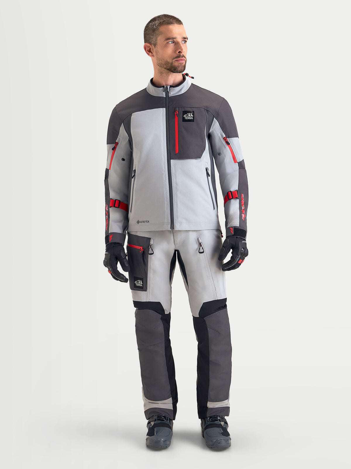 Alpinestars Arenis Gore-Tex uitrustingsset, heren adventure motorkleding in lichtgrijs, donkergrijs en rood, vooraanzicht op model met waterdichte toeruitrusting