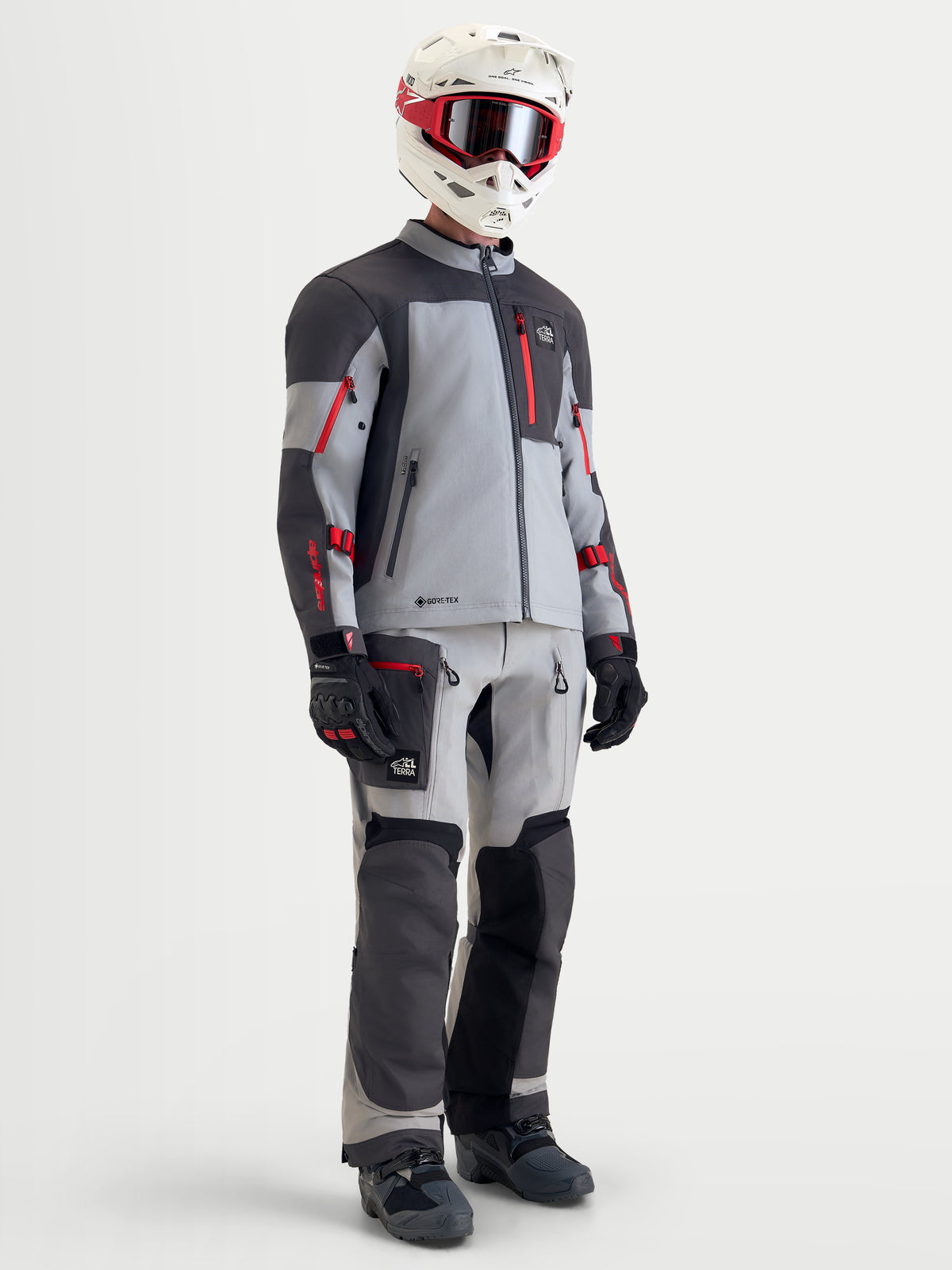 Alpinestars Arenis Gore-Tex uitrustingsset, avontuurlijke motorjas en -brook voor heren in grijs, donkergrijs en rood, volledige weergave op een model met helm, goggle, handschoenen en laarzen, waterdichte all-terrain motorkleding