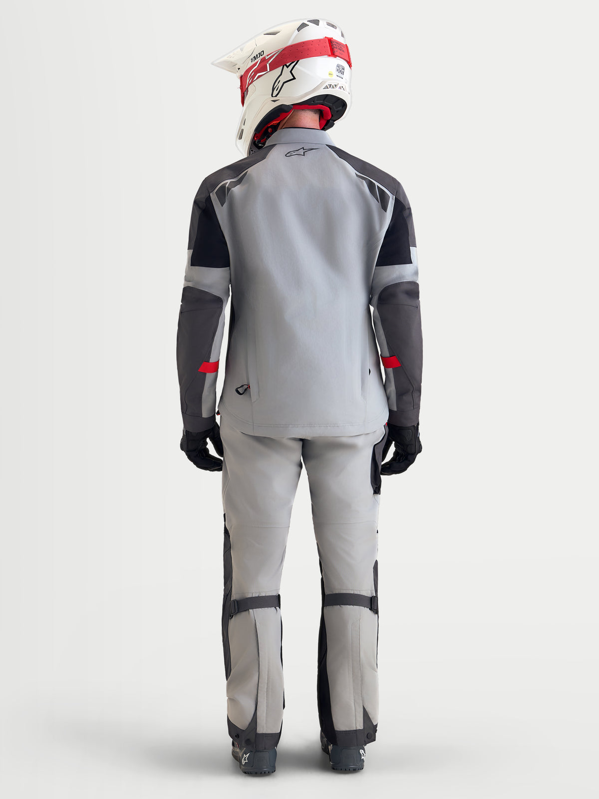 Alpinestars Arenis Gore-Tex uitrustingsset, avontuurlijke motorjas en broek voor heren in lichtgrijs, donkergrijs en zwart, achteraanzicht op model met bijpassende helm en motoruitrusting