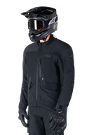 Alpinestars St-7 Prime GORE-TEX jas, zwarte motorjas, gedragen door een rijder met zwarte helm en motorbril, voorzien van grote cargozakken op de borst en een gelamineerde waterdichte buitenlaag, premium uitrusting voor adventure touring en woon-werkverkeer