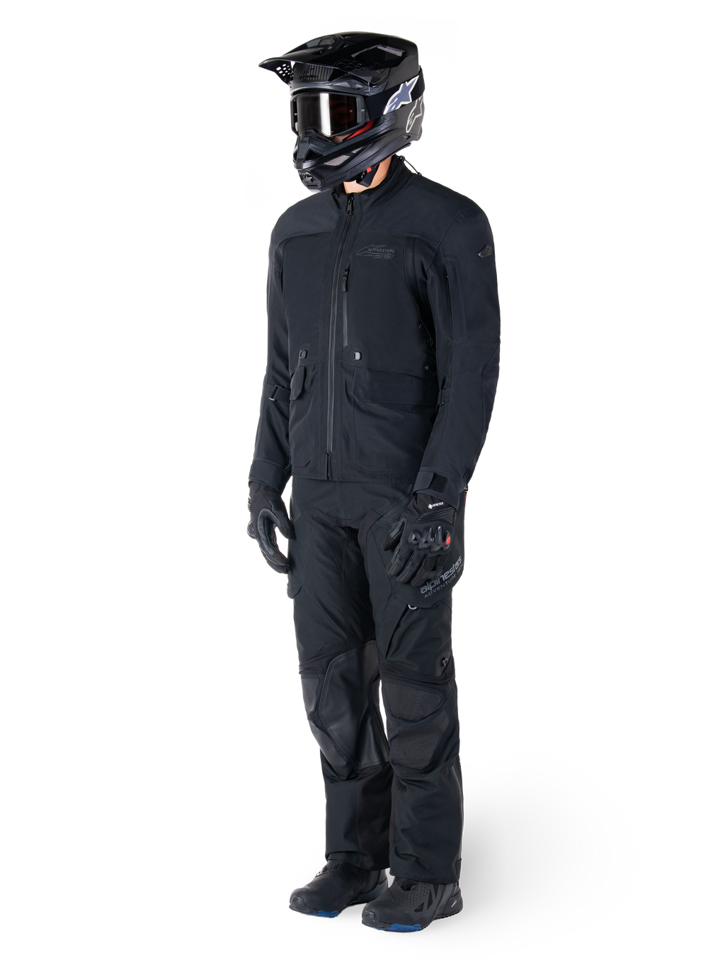 Motorrijder die de Alpinestars St-7 Prime GORE-TEX jas in het zwart draagt, gecoördineerde adventure touring-outfit met bijpassende zwarte broek, zwarte helm met bril en handschoenen, met een gestroomlijnd en functioneel ontwerp voor prestaties onder alle weersomstandigheden.