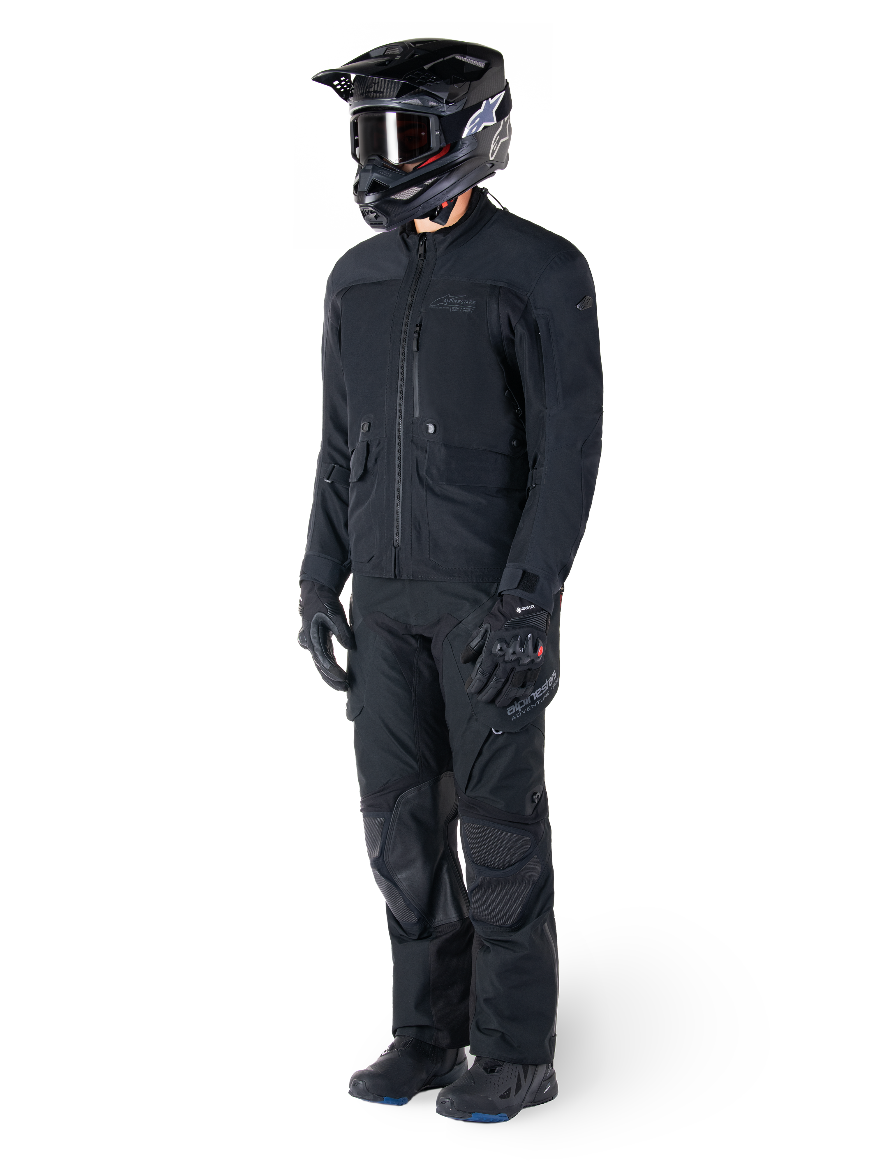Motorrijder die de Alpinestars St-7 Prime GORE-TEX jas in het zwart draagt, gecoördineerde adventure touring-outfit met bijpassende zwarte broek, zwarte helm met bril en handschoenen, met een gestroomlijnd en functioneel ontwerp voor prestaties onder alle weersomstandigheden.
