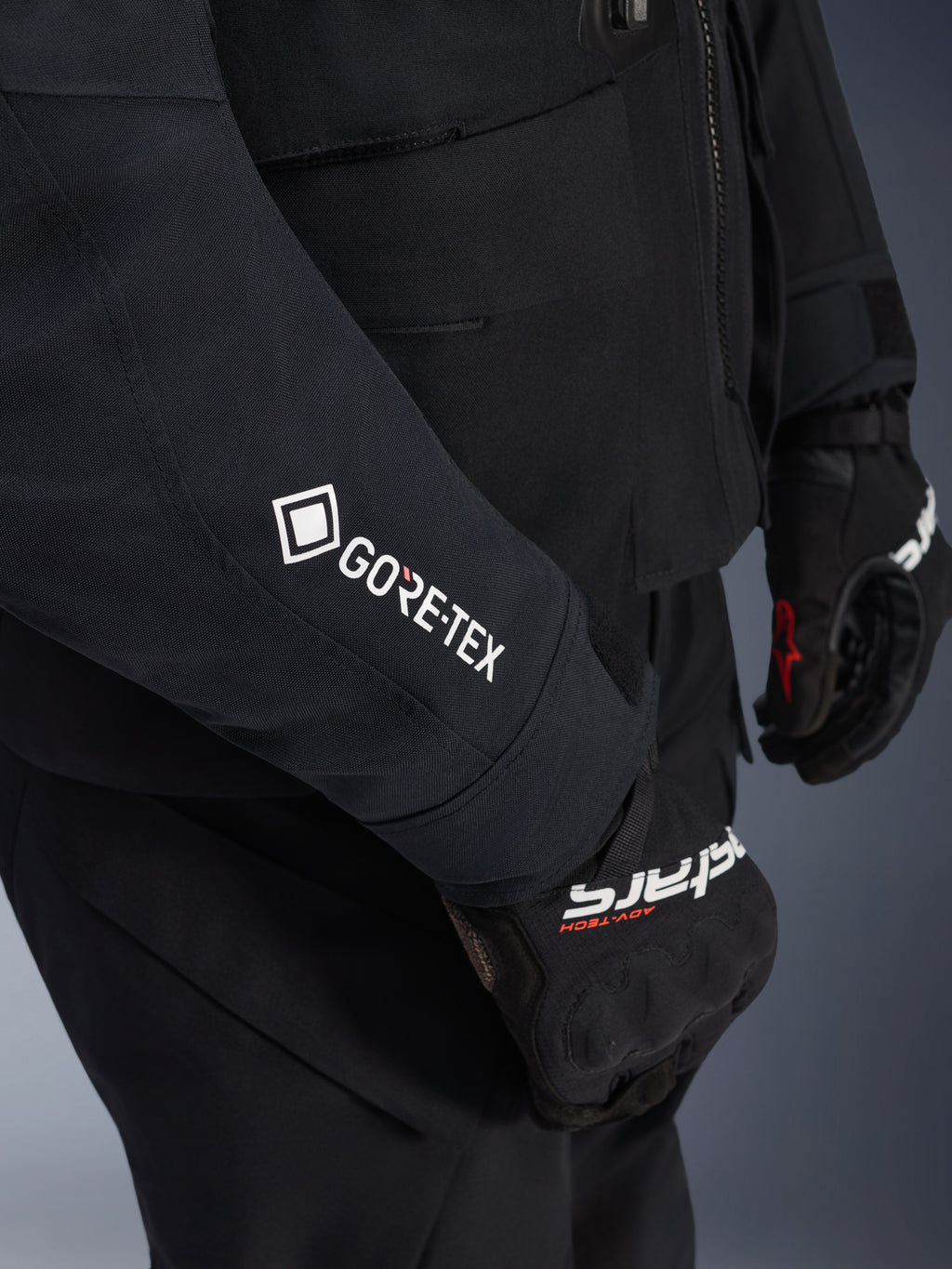 Alpinestars ST-7 2L GORE-TEX Jas, zwart en donkergrijs, close-up van de mouw met witte GORE-TEX-branding, gedragen met zwarte adventure motorhandschoenen, waterdichte motorkleding