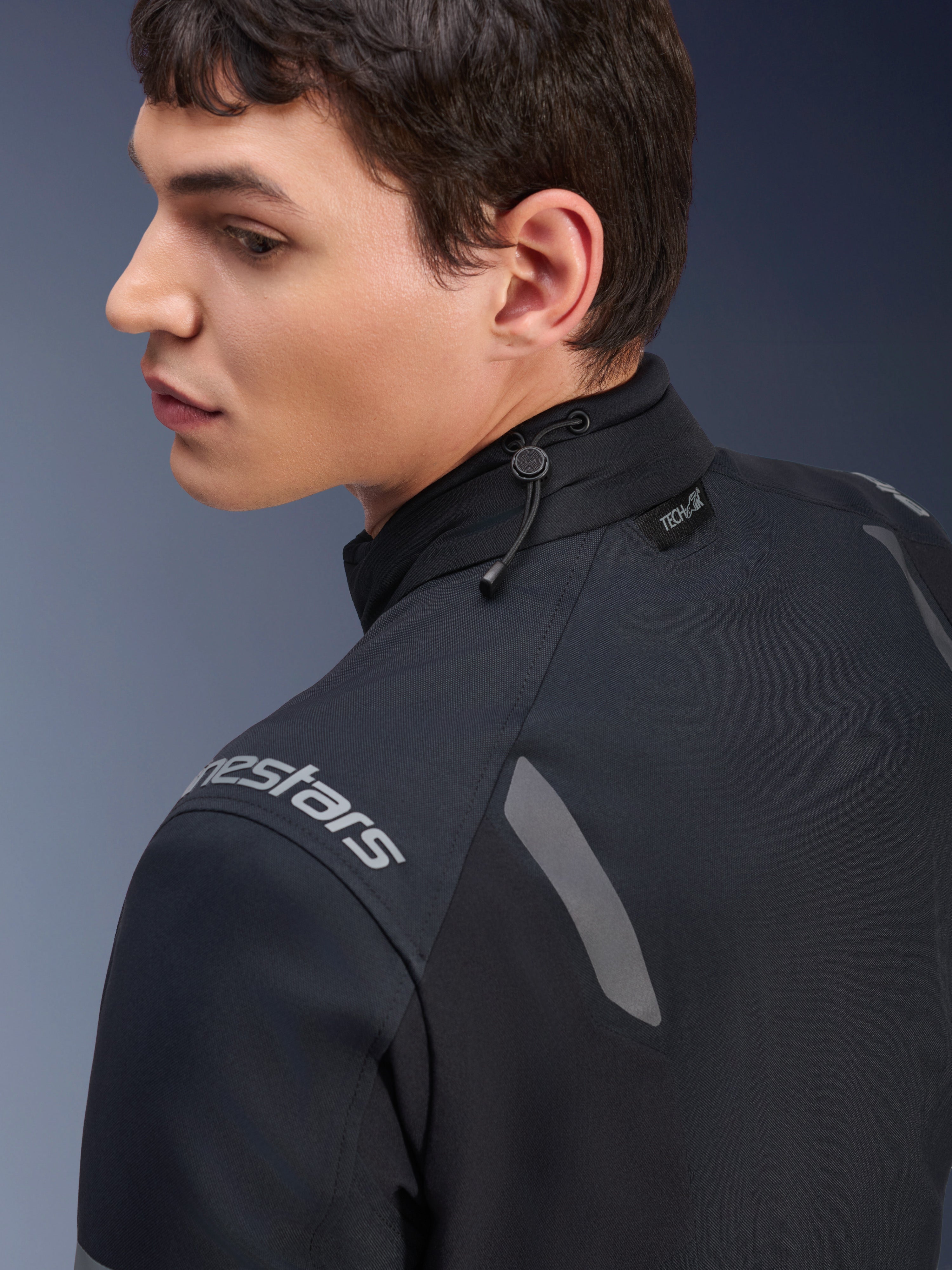 Alpinestars ST-7 2L GORE-TEX Jas, zwarte en donkergrijze motorjas, detailopname van de kraag met het verstelbare schokkoord en Tech-Air label, voorzien van grijze reflecterende accenten en merklogo op de schouder