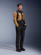 Alpinestars ST-7 2L GORE-TEX Jas, motorjas, Gobi bruin en zwart, gedragen door een model met bijpassende zwarte broek en handschoenen, voorzien van bruine panelen op de borst en mouwen, zwarte technische accenten en oranje logo's, adventure-touring motorkleding.