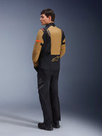 Alpinestars ST-7 2L GORE-TEX jas, adventure motorjas, Gobi bruin en zwart, achteraanzicht op een model met bijpassende motorbroek en laarzen, voorzien van oranje accenten op de mouwen, waterdichte gelamineerde schaal en Alpinestars-logo, ontworpen voor touring en rijden op de weg