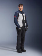 Alpinestars ST-7 2L GORE-TEX jas in de kleuren Ice Gray, donkerblauw en zwart met rode accenten, gedragen door een mannelijk model met zwarte motorbroek en handschoenen, professionele adventure touring motoruitrusting