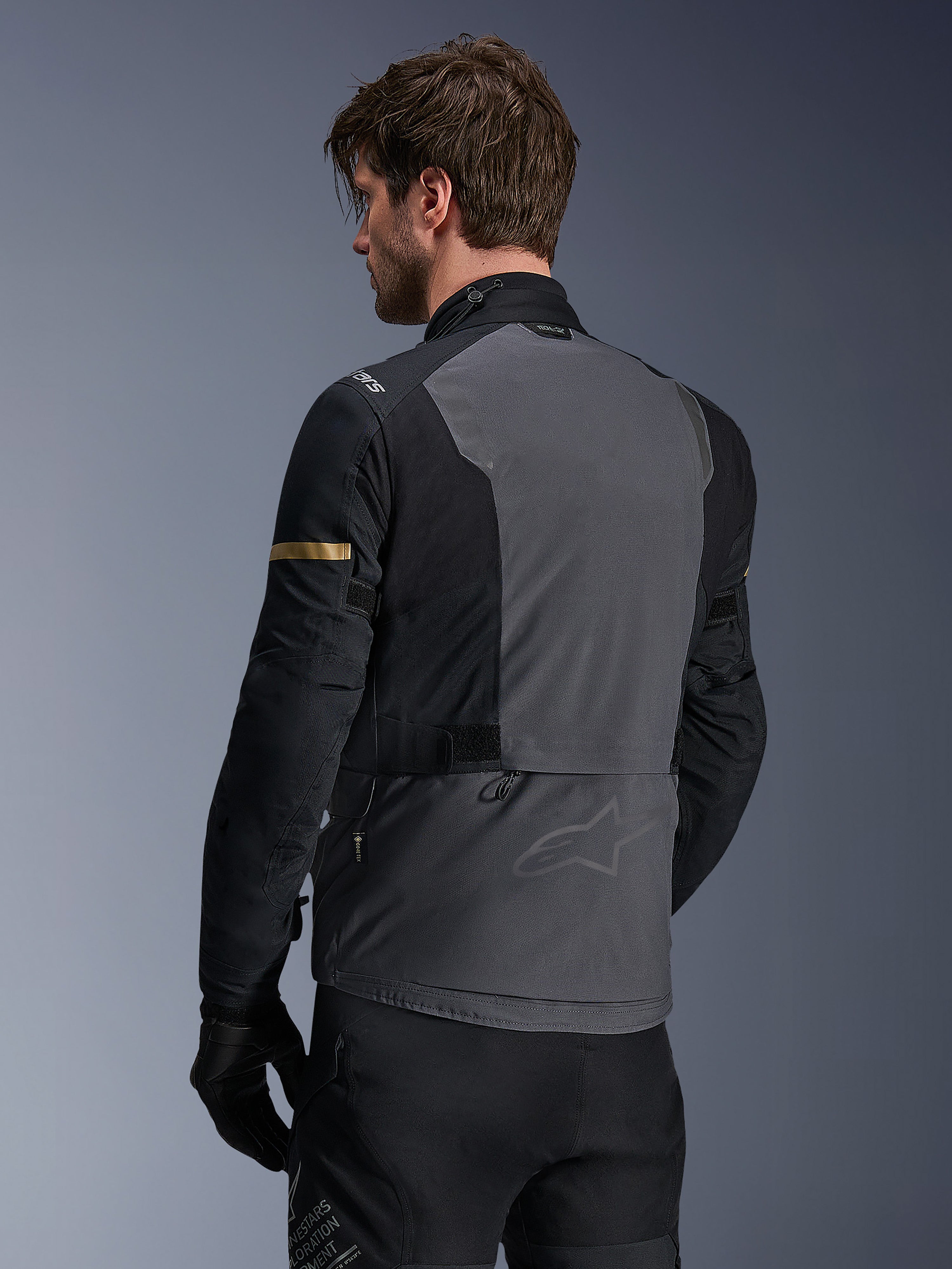 Alpinestars ST-7 2L GORE-TEX Jas, motorjas, donkergrijs, zwart en donkerkhaki, achteraanzicht met groot grijs rugpaneel met subtiele branding, zwarte mouwen met goudkleurige khaki accenten, avontuurlijk waterdicht textielontwerp