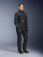 Vrouwelijk model in Alpinestars Stella ST-7 2L GORE-TEX adventure touring-pak, zwart en donkergrijs jack en broek, met opvallende GORE-TEX-branding op de mouw en broekspijp, gecombineerd met zwarte handschoenen en motorlaarzen, professionele motoruitrusting voor touring onder alle weersomstandigheden