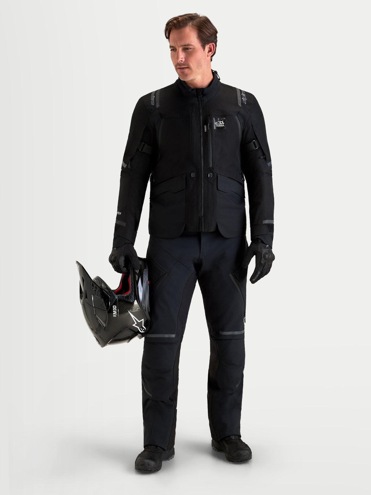 Alpinestars ST-7 V2 2L GORE-TEX broek, heren adventure motorbroek in zwart, vooraanzicht op een model met bijpassende uitrusting en helm, AA-gecertificeerde waterdichte all-terrain motorkleding