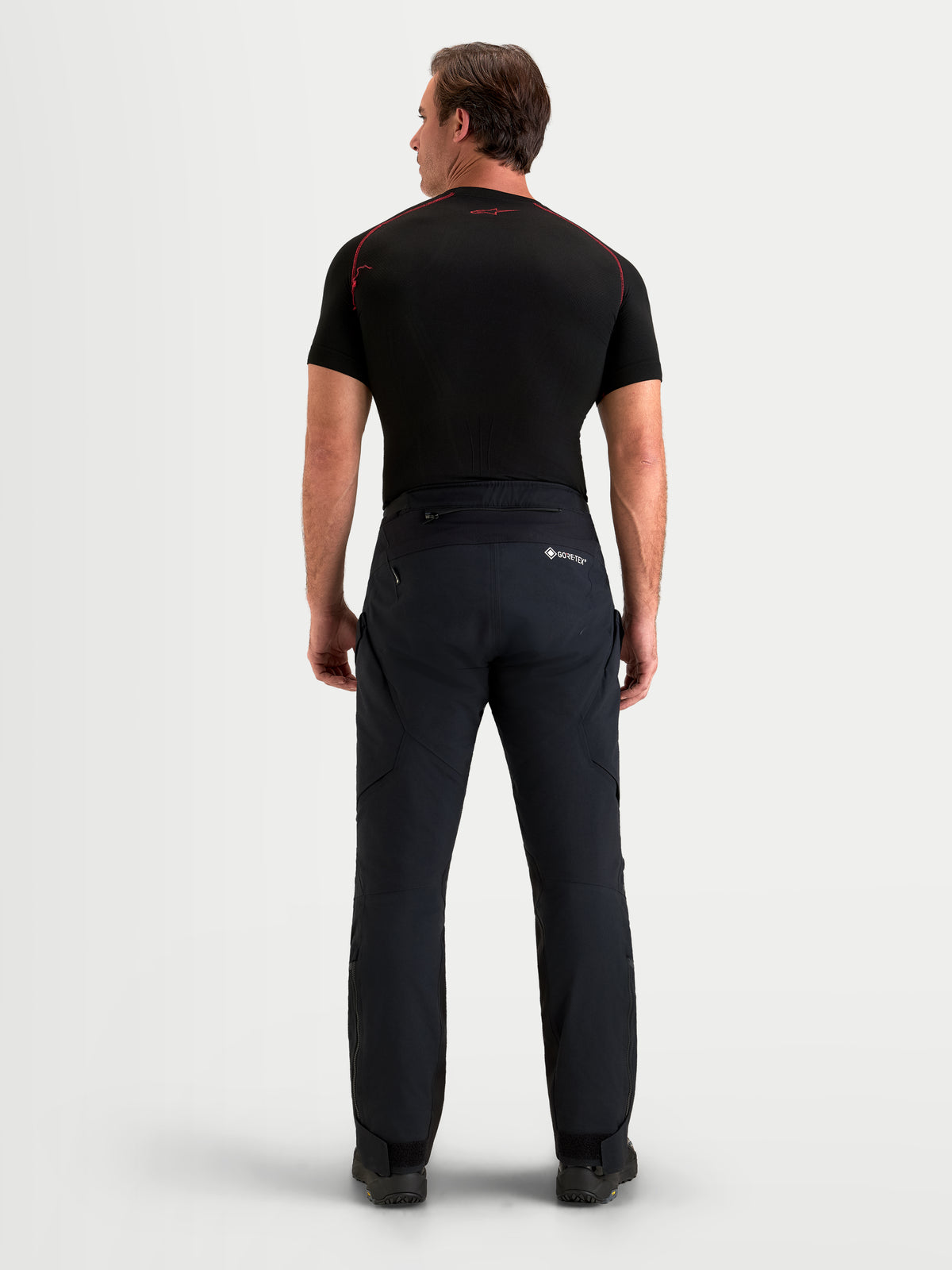 Alpinestars St-7 V2 2L Gore-Tex broek short, heren adventure-motorbroek in zwart, achteraanzicht op model in waterdichte textieluitrusting en bijpassende donkere top
