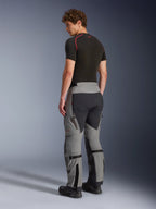 Alpinestars Nazca 3L GORE-TEX PRO broek, adventure motorbroek, donkergrijs en zwart, achteraanzicht van model met een zwarte basislaag en laarzen, toont technische panelen, ventilatieritsen en kuitvolume-verstellers.