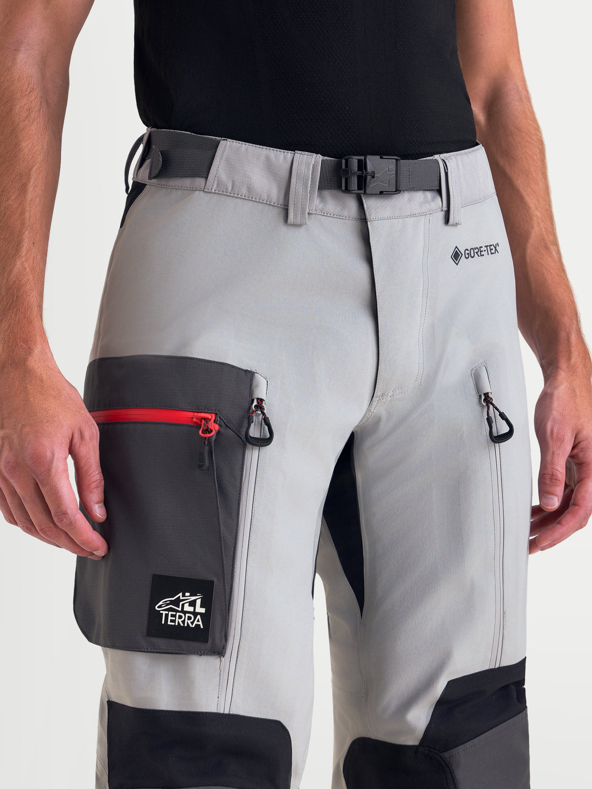 Alpinestars Arenis Gore-Tex Pants, men's adventure touring motorcycle pants in mid gray, deep gray, and black, close-up view showing magnetic waist buckle, GORE-TEX logo, zippered thigh ventilation, and cargo pocket worn by a model.