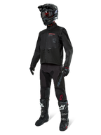 Motocross rider wearing complete racing gear, Alpinestars Pro-Dura Jacket in Black, black pants with grey branding and red accents, black helmet with goggles, and black and white motocross boots, coordinated outfit for enduro and off-road riding