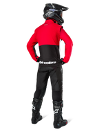 Motocross rider seen from behind wearing the Alpinestars Pro-Dura Jacket in Black, Bright Red, and White, paired with black pants, black helmet, and black off-road boots, featuring a red upper and black lower section with white Alpinestars branding across the back.