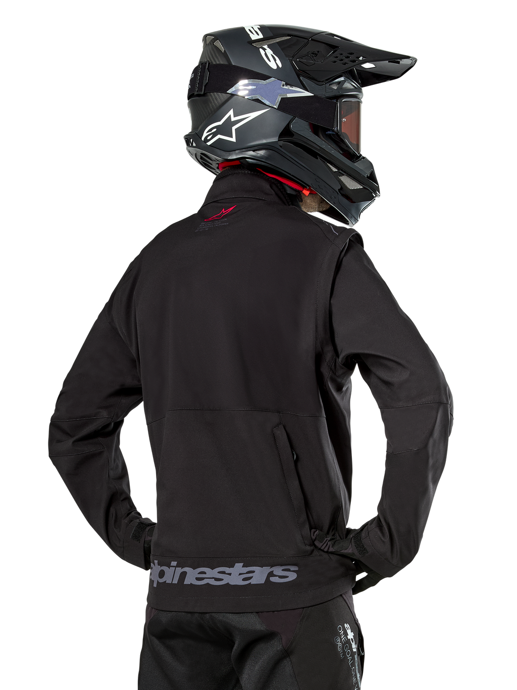 Alpinestars Lite-Dura Softshell Jas, zwart, rugaanzicht gedragen door een rijder, met grijze Alpinestars-branding op de achterzoom en een klein rood logo op de kraag, gecombineerd met een zwarte motorcrosshelm, ontworpen voor enduro- en off-road rijden.