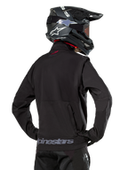 Alpinestars Lite-Dura Softshell Jas, zwart, rugaanzicht gedragen door een rijder, met grijze Alpinestars-branding op de achterzoom en een klein rood logo op de kraag, gecombineerd met een zwarte motorcrosshelm, ontworpen voor enduro- en off-road rijden.