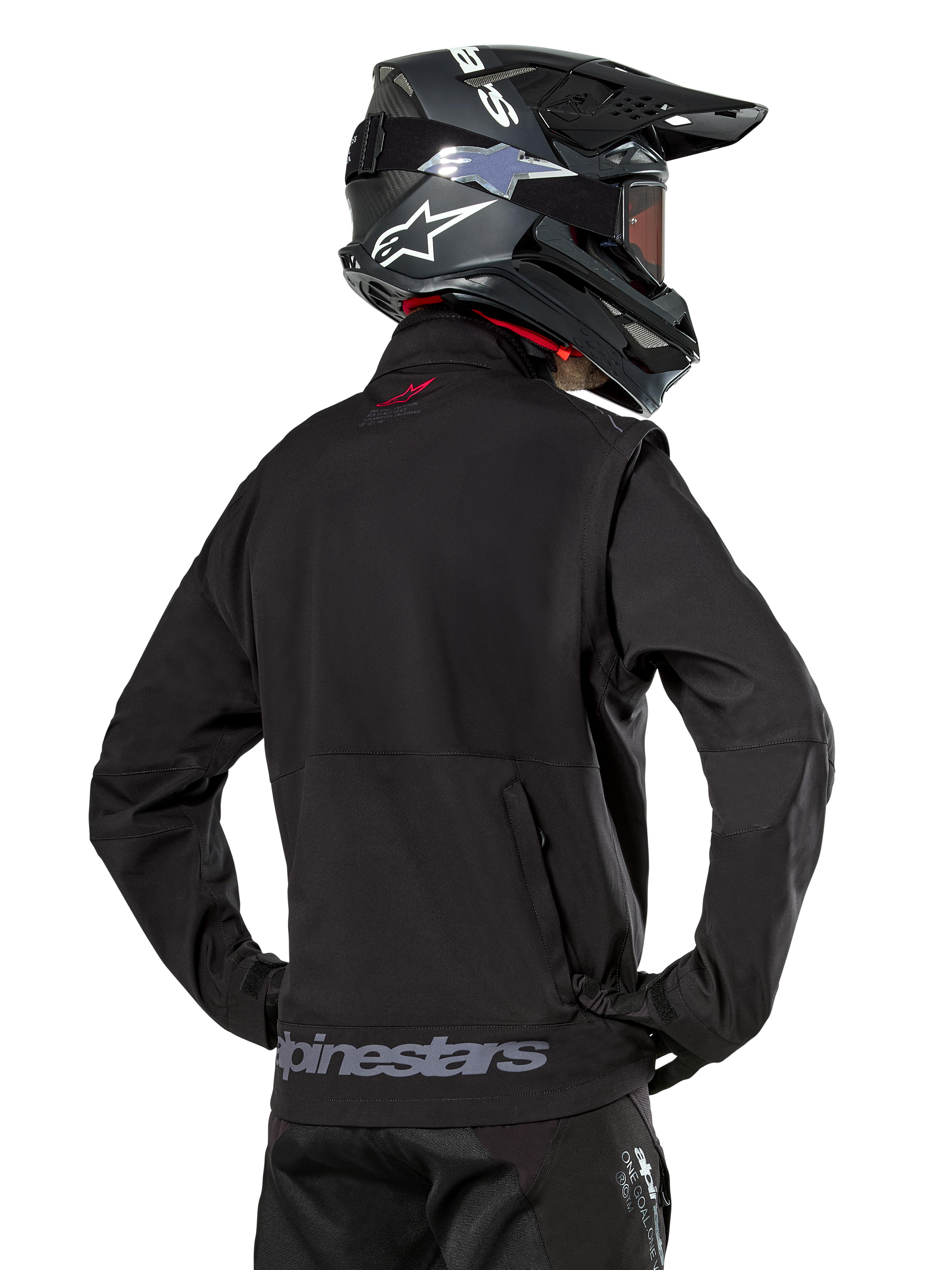 Alpinestars Lite-Dura Softshell Jas, zwart, rugaanzicht gedragen door een rijder, met grijze Alpinestars-branding op de achterzoom en een klein rood logo op de kraag, gecombineerd met een zwarte motorcrosshelm, ontworpen voor enduro- en off-road rijden.