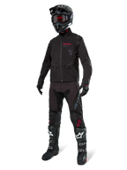 Alpinestars Lite-Dura Softshell Jas, zwart, gedragen door een mannequin als onderdeel van een complete off-road uitrusting met zwarte broek, zwart-witte laarzen en zwarte helm met rode bril, professionele motorcross- en enduro-kleding