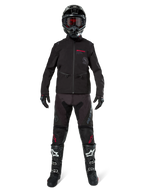 Motorcrossrijder in de Alpinestars Lite-Dura Softshell Jas in zwart met rode logo-details, gestyled met bijpassende zwarte off-road broek, zwarte helm en zwart-witte laarzen, complete professionele enduro race-uitrusting.