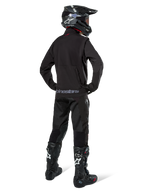 Enduro-rijder van achteren gezien in de Alpinestars Lite-Dura Softshell Jas in het zwart, gecombineerd met een zwarte technische rijbroek en laarzen, voorzien van een achterzak met ritssluiting en Alpinestars-logo op de onderste zoom, complete off-road uitrusting voor motorcross