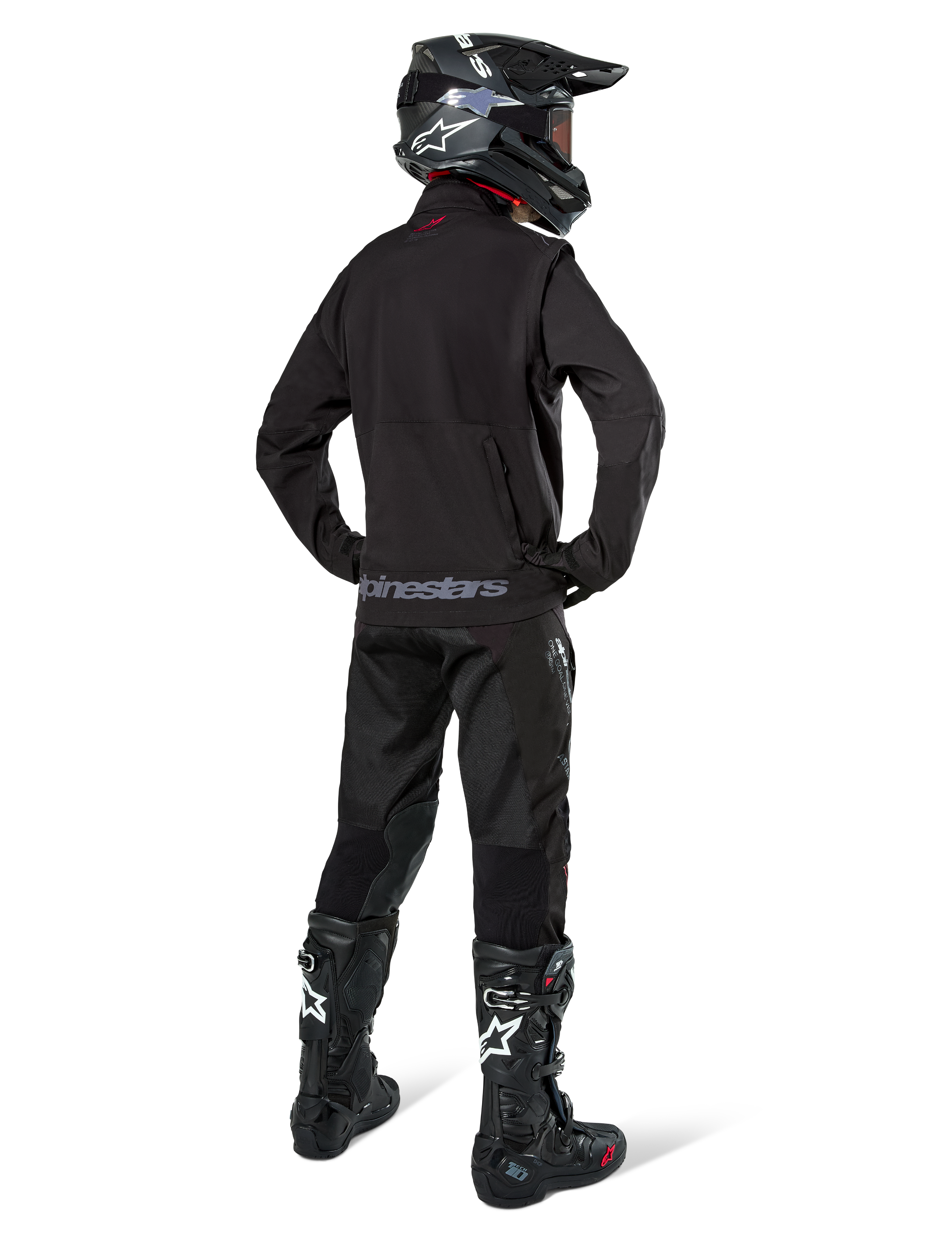 Enduro-rijder van achteren gezien in de Alpinestars Lite-Dura Softshell Jas in het zwart, gecombineerd met een zwarte technische rijbroek en laarzen, voorzien van een achterzak met ritssluiting en Alpinestars-logo op de onderste zoom, complete off-road uitrusting voor motorcross