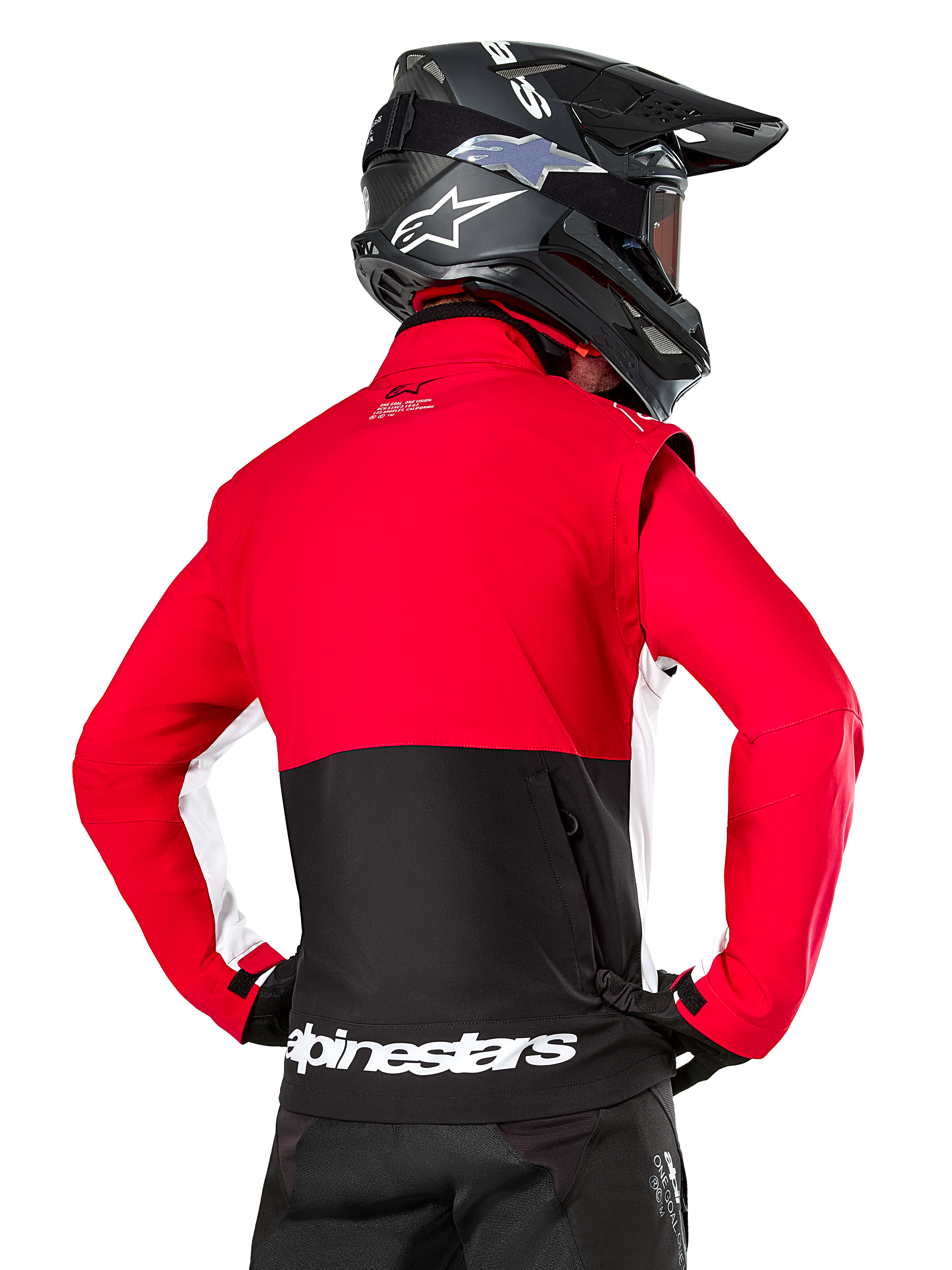 Alpinestars Lite-Dura Softshell Jacket, Black Bright Red White, achteraanzicht op een motorcrosser, rood bovenstuk en mouwen met een zwart paneel op de onderrug, opbergzak met rits op de rug, wit Alpinestars-logo op de onderste zoom, gedragen met een zwarte helm en broek