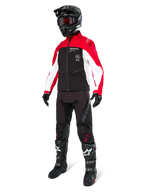 Motorcrossrijder in de Alpinestars Lite-Dura Softshell Jas in zwart, felrood en wit, met een zwart lijf en rood-witte mouwen, gecombineerd met een zwarte broek, een zwarte helm met een rode bril en zwart-witte laarzen, complete off-road race-uitrusting.